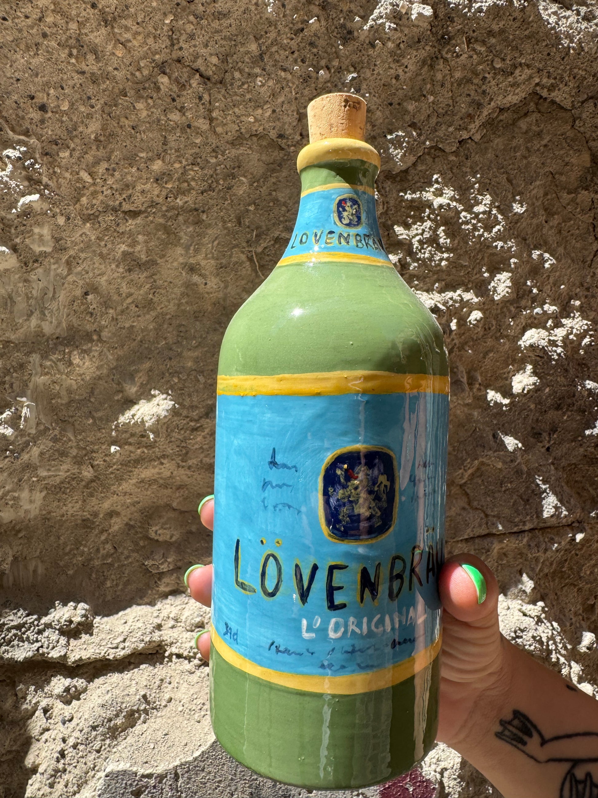 Scarico di Lovembrau di Oilloc2, bottiglia con etichetta verde e gocce di olio naturale, su sfondo bianco.